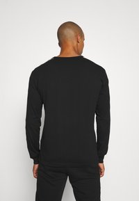 Schwarzes Langarmshirt mit Rundhalsausschnitt, das eine glatte Textur und subtile Nähte entlang der Schultern aufweist.