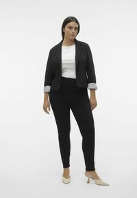 Veste noire avec des poignets rayés, haut blanc, pantalon noir et escarpins crème à bout pointu. Design simple avec une coupe ajustée et des lignes épurées.