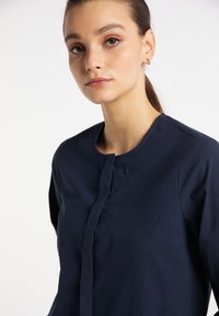 Marineblå skjorte med rund halsudskæring, knaplukning foran og lange ærmer. Glat tekstur og skræddersyet pasform er synlige.