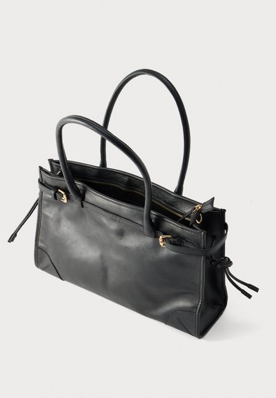 Sac fourre-tout en cuir noir avec deux poignées, boucles en métal doré, une fermeture éclair sur le dessus et des détails à cordon latéral sur fond blanc.