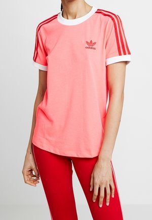 Lyserød bomulds t-shirt med hvid krave og røde Adidas-striber på ærmerne; har et lille rødt logo på venstre bryst.