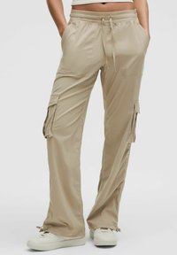 Beżowe spodnie cargo wykonane z lekkiego materiału, z elastycznym pasem, bocznymi kieszeniami i luźnym krojem o prążkowanej teksturze.