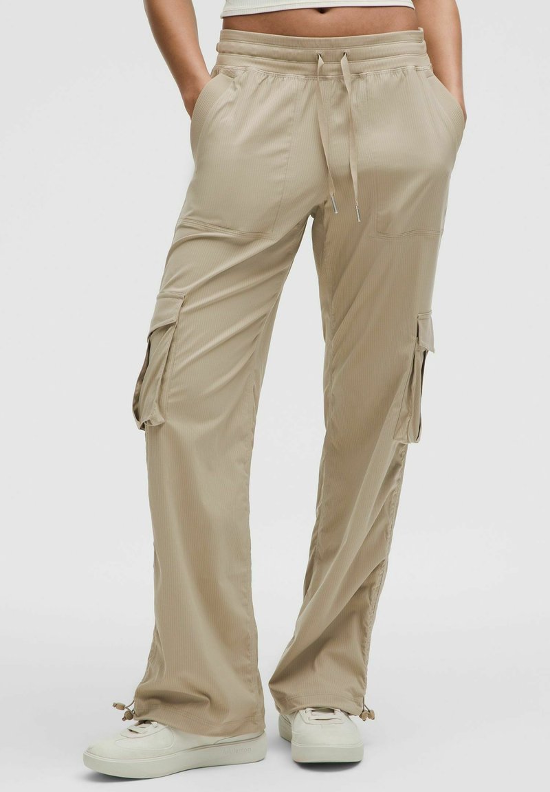 Beżowe spodnie cargo wykonane z lekkiego materiału, z elastycznym pasem, bocznymi kieszeniami i luźnym krojem o prążkowanej teksturze.
