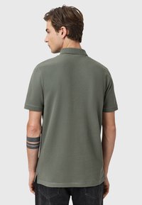 Olivgrünes Polohemd mit kurzen Ärmeln. Mit einem Kragen, seitlichen Schlitzen am Saum und einer glatten, atmungsaktiven Textur.