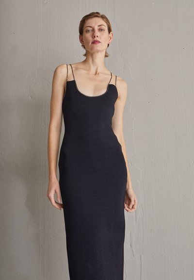 Must läikiv must kleit, ilma varrukateta, ümmarguse kaelusava ja õhukeste rihmadega, millel on vormiv siluett ja kesksetel põlvedel ulatuv pikkus.