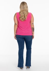 Fuchsia mouwloze top met een gladde textuur, gecombineerd met uitlopende blauwe jeans. De outfit heeft een strakke silhouet zonder opvallende patronen.