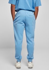 Ljusblå sweatsbyxor i mjukt material, med en bakficka och avsmalnande anklar, i kombination med vita sneakers.