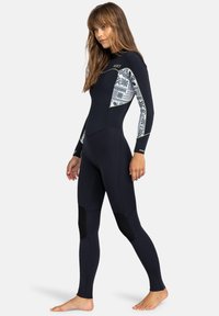 Survêtement en néoprène noir avec des panneaux latéraux à motifs, des manches longues, un col haut et des accents renforcés aux genoux pour plus de durabilité et de confort.