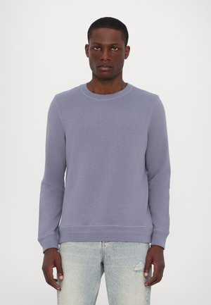 Sweatshirt violet deschis cu guler rotund, mâneci lungi și mansete și tiv cu tricot. Material moale cu o textură subtilă, asortat cu blugi albaștri.
