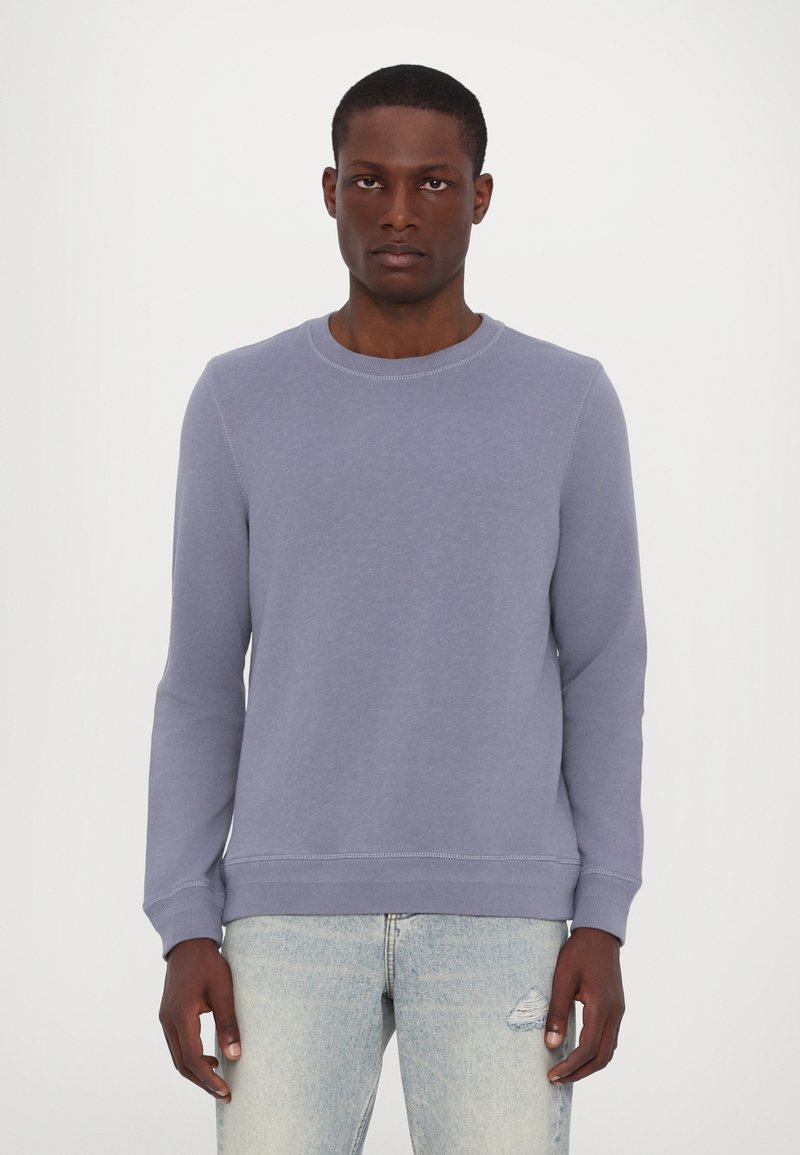 Sweatshirt violet clair à col rond, manches longues et bords-côtes aux poignets et à l'ourlet. Tissu doux avec une texture subtile, associé à un jean bleu.