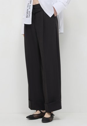 Pantaloni neri a gamba larga con una superficie liscia, dotati di risvolto, passanti per cintura e una cintura abbinata per la chiusura. Abbinati a ballerine.