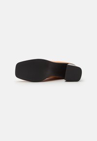 Zapato de tacón naranja con suela de goma negra texturizada. Cuenta con una puntera cuadrada y un tacón bloque moderado. Material superior suave, con un detalle mínimo.