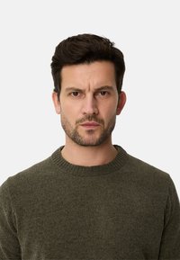 Mørkegrøn strikket sweater med rund halsudskæring, tekstureret stof og løs pasform, der har en glat overflade og subtile variationer.