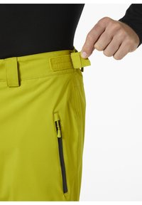 Limetkové kalhoty s úpravou v pase na suchý zip a boční kapsou na zip; hladká textura, zúžený střih a odolná látka.