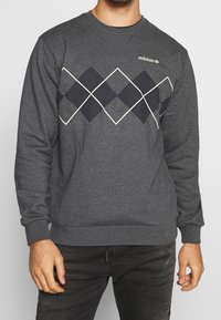 Grå sweatshirt med rund hals, med ett diamantmönster i marinblått som är konturerat i vitt och en Adidas-logotyp på bröstet.