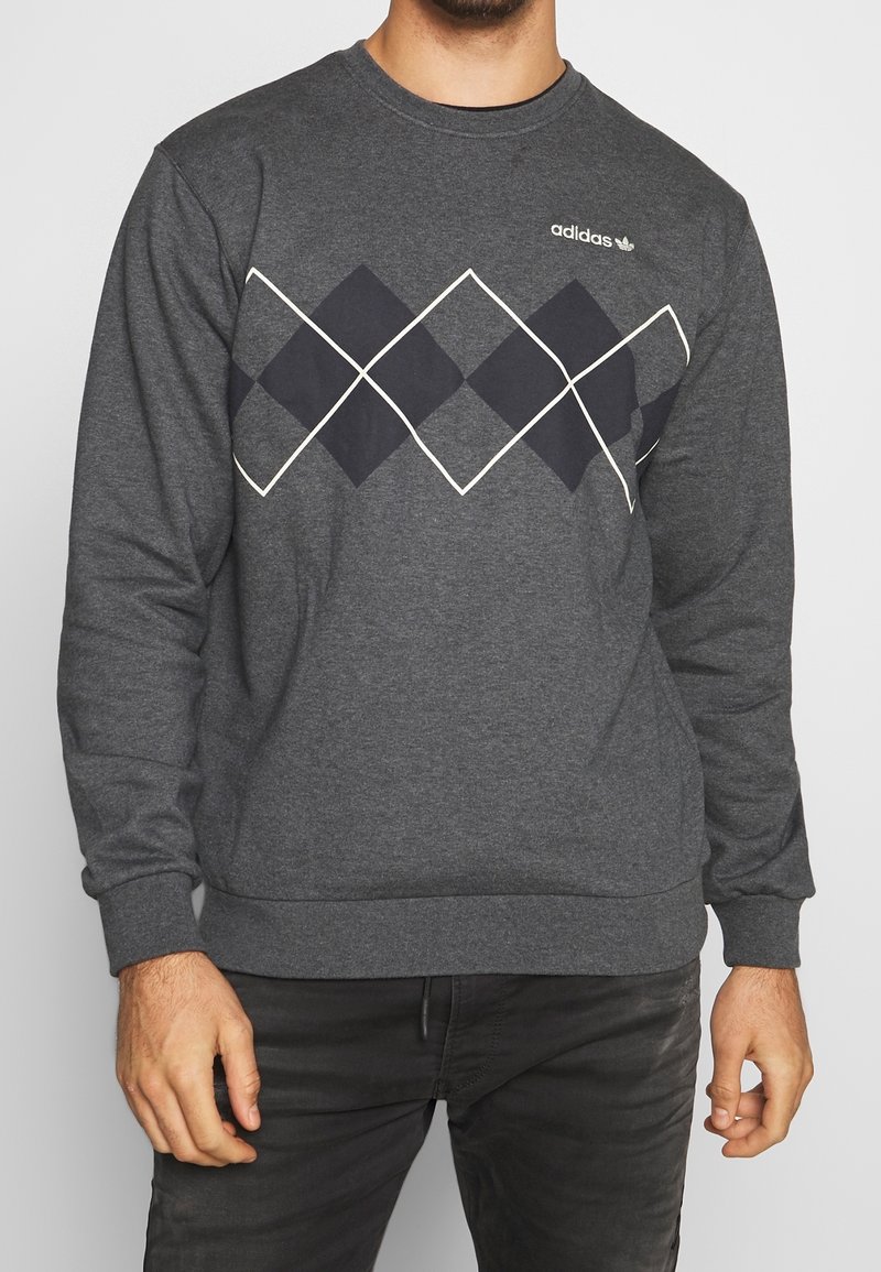 Grå sweatshirt med rund hals, med ett diamantmönster i marinblått som är konturerat i vitt och en Adidas-logotyp på bröstet.
