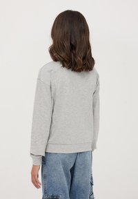 Szary bawełnowy sweter z długimi rękawami, ściągaczami przy mankietach i u dołu, charakteryzujący się prostym, nieozdobnym wzorem. Noszony z niebieskimi dżinsowymi spodniami cargo.