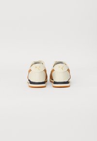 Hvite og brune sneakers med strukturert overflate, med svart såle og gulllogo på baksiden. Lave sko.