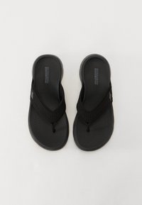 Black flip-flops with a textured rubber sole and woven fabric straps. Features a thong design and logo on the footbed.