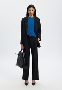 Melns žakets virs zila džemperī, kopā ar melnām biksēm. Iekļauj strukturētu melnu somu un smailus melnus zābakus. Gludas tekstūras.