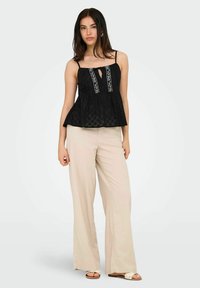 Czarny top peplum na cienkich ramiączkach, z teksturowanej tkaniny, z wycięciem w kształcie klucza i białym haftem kwiatowym na środku; zestawiony z beżowymi spodniami typu wide-leg.