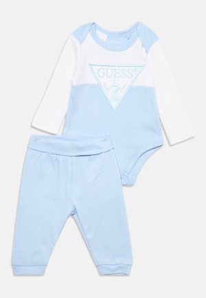 Ensemble bébé avec pantalon bleu clair et body à manches longues blanc et bleu clair avec logo Guess.