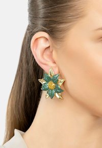 Gold-tone flower-shaped earring featuring green glitter petals and a yellow center. Smooth and textured surfaces enhance visual contrast.