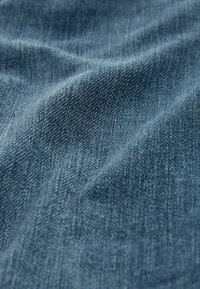 Tissu en denim d'une teinte bleu moyen avec une texture subtile et un motif de tissage diagonal, présentant de douces ondulations et plis.