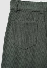 Pantaloni in corduroy verde scuro che mostrano tasca posteriore, passanti per cintura e texture a coste verticali.