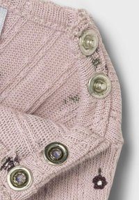 Vêtement tricoté rose clair présentant des motifs texturés et des boutons-pression métalliques avec des accents colorés le long du bord.