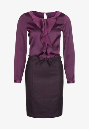 Violetti pusero, jossa on röyhelö etuosassa ja pitkät hihat, yhdistettynä tiukkaan tummanviolettiin hameeseen, jossa on kangasvyö vyötäröllä.