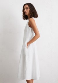 Robe sans manches en lin blanc avec un design évasé, des poches latérales et une texture lisse, tombant en dessous du genou.