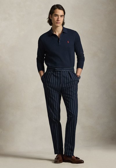 Navy long-sleeve polo shirt with small logo, paired with navy pinstriped trousers. Brown shoes and a watch complete the outfit.