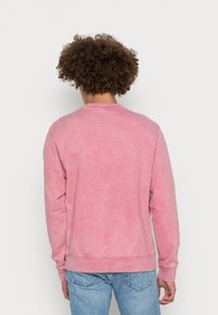 Sweatshirt rose avec une apparence fanée et texturée. Encolure et poignets côtelés, manches longues et coupe décontractée. Associé à un jean bleu clair.