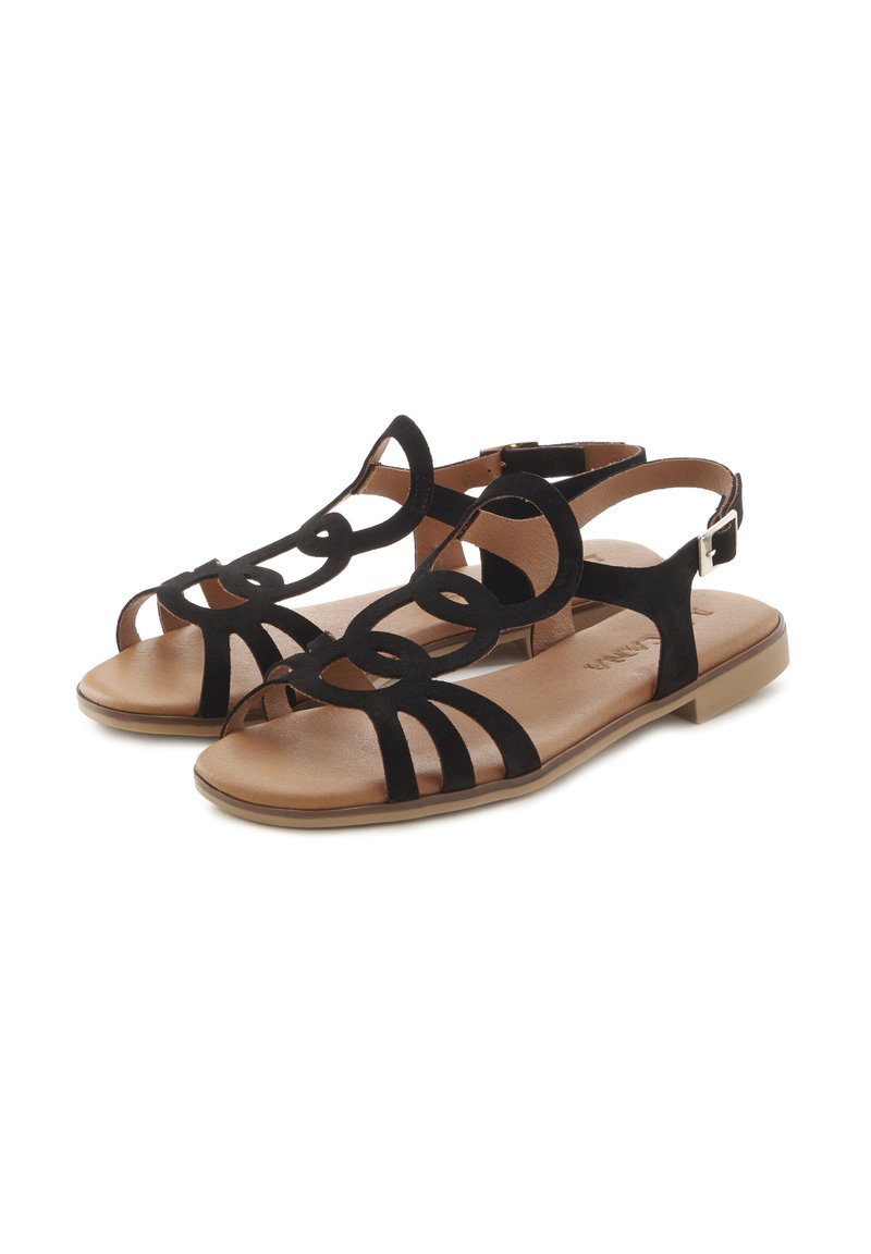 Black suede sandals with geometric cut-out design, flat sole, and tan footbed. Features buckle strap for adjustment and stability.