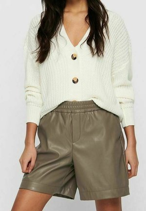 Femme portant un pull en tricot blanc avec de gros boutons et un short en cuir marron taille haute, longueur genou.