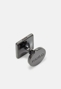 Gemelli in metallo nero con retro quadrato e frontale circolare, stampato con "HUGO." Superficie liscia con finitura riflettente.