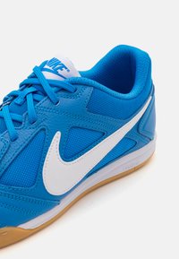 Modra športna čevlja z mrežastimi in usnjenimi materiali. Ima bel Nike znak, teksturirano površino in gumijast podplat.