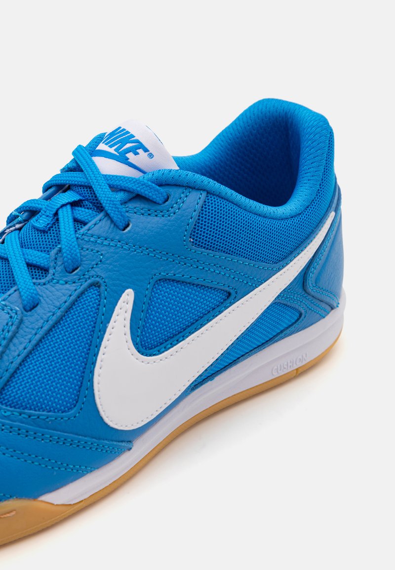 Zapatilla deportiva azul con materiales de malla y cuero. Presenta un swoosh blanco de Nike, una superficie texturizada y una suela de goma.