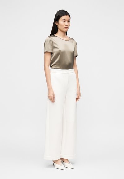 Top de manga curta em verde-oliva acetinado combinado com calças brancas de perna larga, apresentando uma textura suave e um detalhe subtil na bainha.