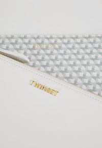 Portefeuille blanc avec le logo doré "TWINSET", présentant un intérieur gris à motif pied-de-poule. Texture lisse et fermeture zippée.