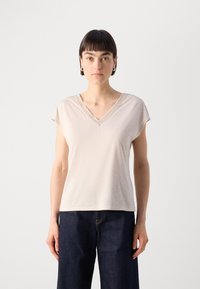 Beige V-hals T-shirt met korte mouwen, voorzien van een textuurafwerking rond de halslijn, gecombineerd met donkerblauwe wijde jeans.