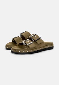 Olivgrüne Wildledersandalen mit zwei verstellbaren Riemen, metallischen Schnallen und schwarzen Gummisohlen, die am Rand mit silbernen Nieten verziert sind.