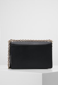 Borsa a tracolla in pelle nera con catena, forma rettangolare, superficie testurizzata, hardware color oro, caratterizzata da un design elegante e minimal.