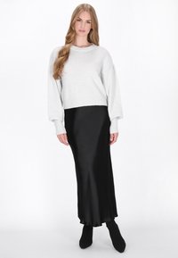 Jasnoszary, dziany sweter z balonowymi rękawami, zestawiony z czarną, satynową spódnicą maxi. Modelka nosi czarne botki za kostkę. Widoczna gładka struktura materiału.