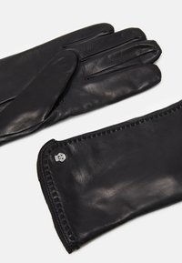 Schwarze Lederhandschuhe mit glatter Textur, elongated Design und dekorativem Nähen entlang des Bündchens; verfügen über ein kleines metallisches Logo-Element.