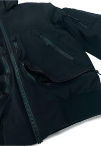 Schwarze, wasserdichte Jacke mit mehreren Reißverschlüssen, gerippten cuffs und strukturiertem Stoff. Zwei Seitentaschen und eine Brusttasche mit Reißverschluss.