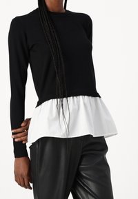 Czarny sweter dzianinowy z długimi rękawami, z białym falbaniastym dołem. Noszony z czarnymi skórzanymi spodniami. Gładka tekstura, casualowy styl.