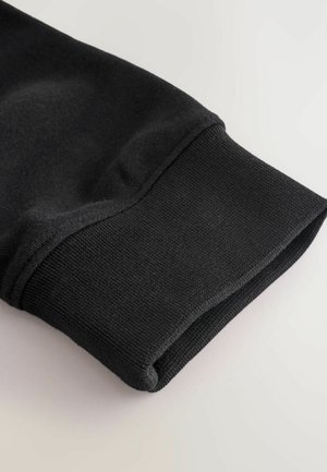 Black cotton sweater cuff with ribbed texture, folded edge, and smooth inner lining. No patterns or hardware visible.