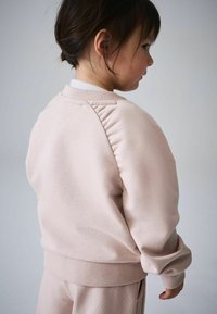 Világos rózsaszín pulóver puha anyagból, bordázott szegéllyel és puffadt vállrészlettel. Sima textúrájú, kerek nyakkivágással.